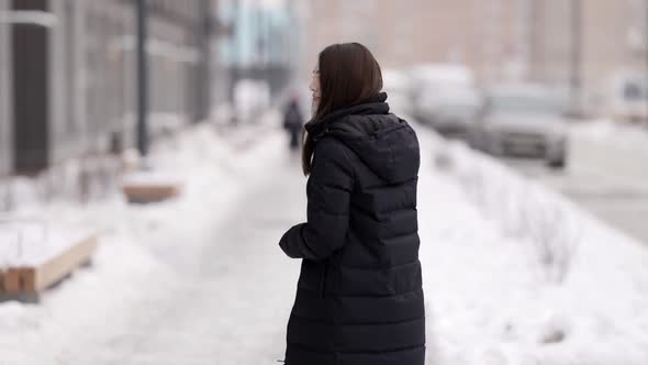 A Young Beautiful Darkhaired Woman Walks Through a Snowcovered City Enjoying a Beautiful Winter Day