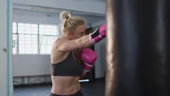Caucasian female boxer wearing boxing gloves training with punching bag at the gym