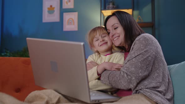 Mother and Small Child Daughter Kid Study at Laptop Watching Funny Movies Relaxing Lying on Sofa