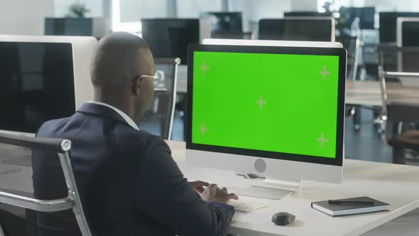 Business AfricanAmerican Man Working on Desktop Computer with Green Screen Mock Up Display in Busy