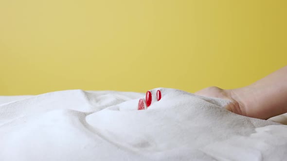 Woman's Hand Scoops Up and Sprinkles White Sand on Yellow Studio Background