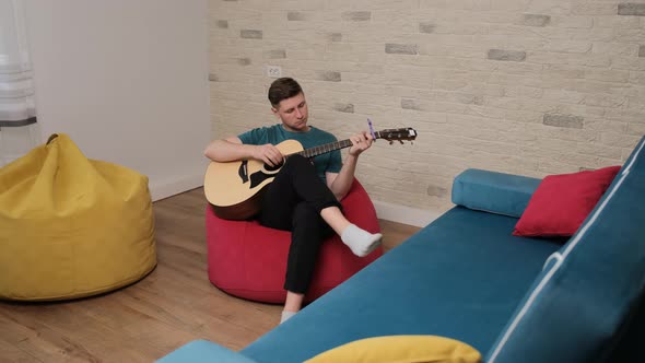 Young Artist Sitting on Red Bean Bag and Playing at the Guitar