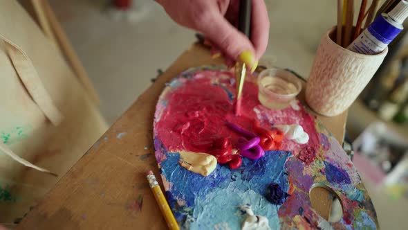 Female Artist with Thick Paintbrush is Mixing Different Coloured Oil Paints on Palette Purple Red