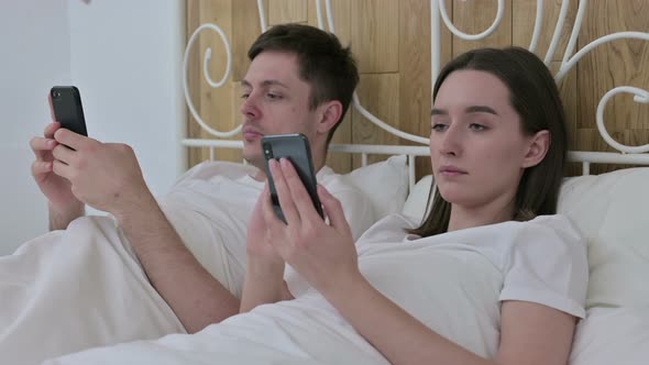 Attractive Young Couple Using Smartphone in Bed 