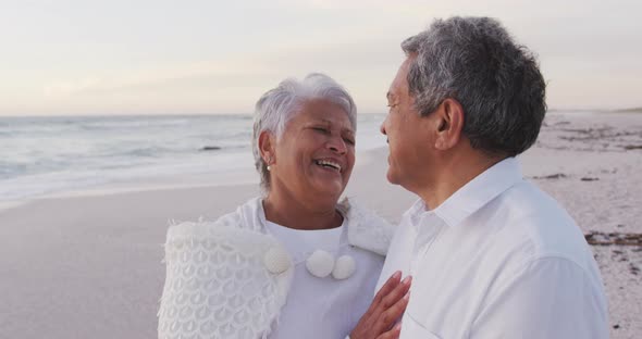 Happy hispanic senior couple embracing and laughing on beach at sunset