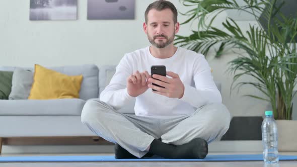 Man Using Smartphone on Yoga Mat at Home