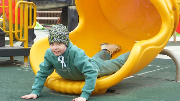 playful caucasian boy 7 years old rides down a tube slide in an amusement park on a sunny day. slow 