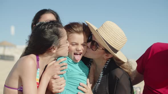 Front View of Happy Family Sitting Together on Beach and Kissing