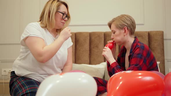 Lgbt Couple in Bed Cheerfully Inflate Balloons Inflated in the Form of a Heart Lie Nearby