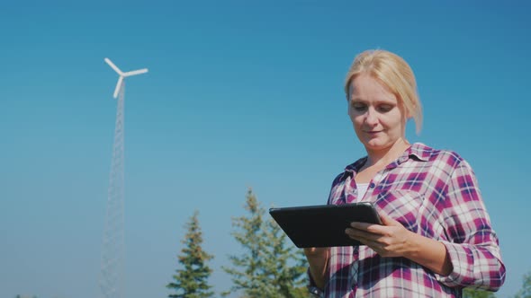A Young Woman Uses a Tablet, in the Background Running a Home Wind Power Station