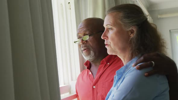 Happy senior diverse couple wearing shirts and embracing in living room