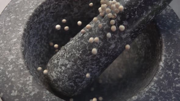 Closeup of Spicy Exotic White Peppercorns Falling Into the Grey Stone Mortar