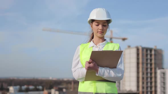 Portrait of Young Woman Engineer Who is Making Entries in Documents