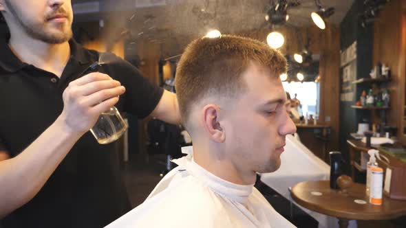 Young Hairstylist Spraying Water on Male Hair From Sprayer After Cutting in Barbershop. Hairdresser