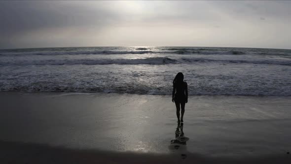 The silhoutte of a woman walking into the ocean during sunset