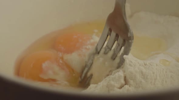 Macro shot mixing egg yolks into flour with fork