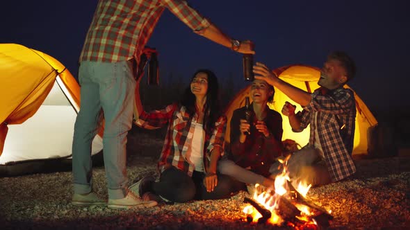 Young Adult Man in Casual Wear Brings Four Bottles of Beer To His Friends at Bonfire in Beach