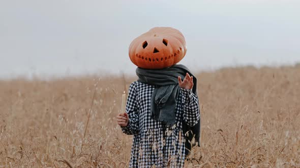 Funny Little Teenage Girl in a Giant Pumpkin Head with a Candle in Her Hand Greets and Waves at the