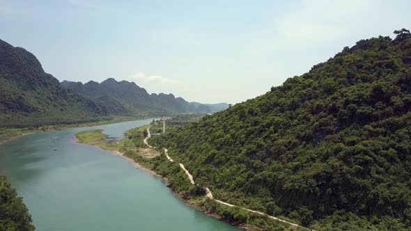 Calm River Runs Between Mountain with Road and Fields Aerial