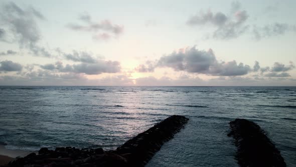 Fly up over a morning beach revealing golden sunrise reflecting off the calm ocean, aerial