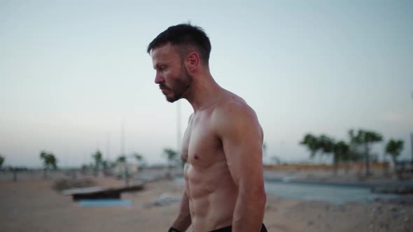 Handsome muscular man getting ready to flip big tire in outdoor beach gym.