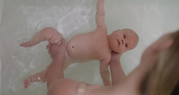 Top View of Funny Newborn Baby Swimming During Bathing with Mother's Help