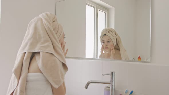 Teenage girl applying moisturizer to her face in front of the bathroom mirror