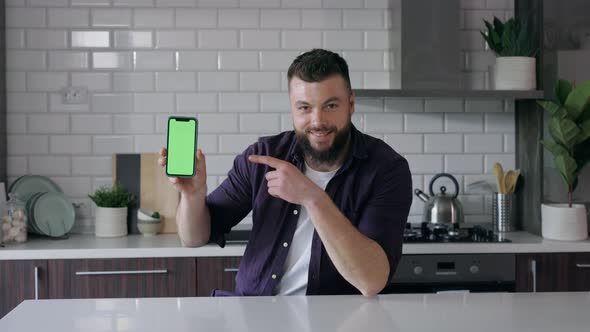 Smiling Man holding a Smartphone with Green Screen and Pointing, Kitchen, Copy Space