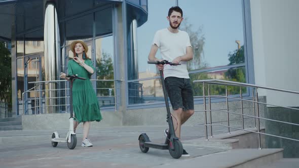 Happy Couple Walks Down Stairs with Electric Scooters on City Area in Summer