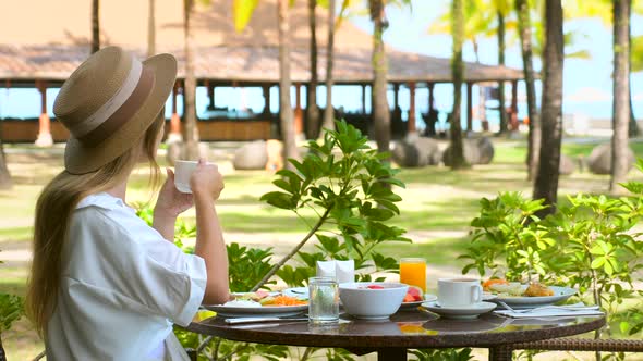 Young Woman Drinking Hot Coffee in White Cup at Outdoor Luxury Resort Restaurant