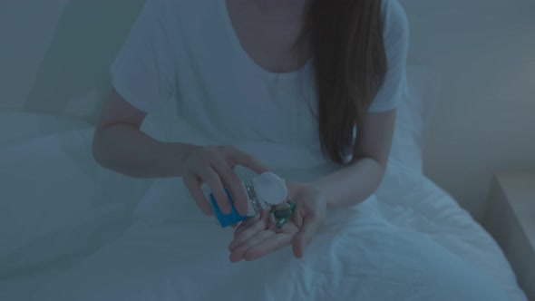 Asian unhappy sick girl in pajamas take medicine before sleep on bed.