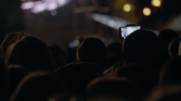 View From Behind of Hands Hold Camera with Digital Display Among People at Rave Party with Light