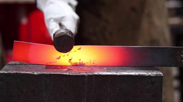 Blacksmiths forging hot metal with hammer in workshop