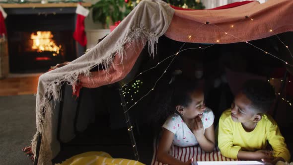 Happy african american siblings using tablet in makeshift tent