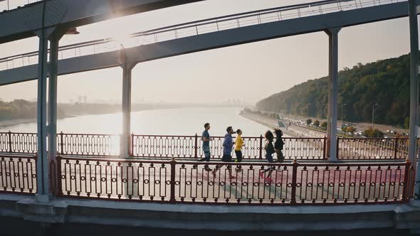 Morning Workout Concept Side View From Drone at Group of Five Runners Training on Bridge Early in