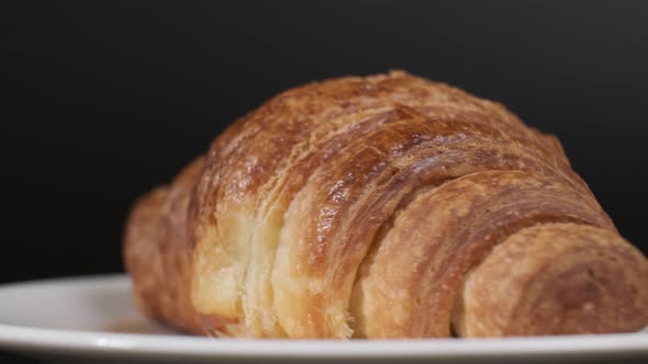 Croissant on white plate rotating in front of camera on black background