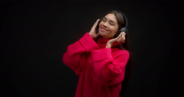 Beautiful Woman in a Bright Pink Sweater Enjoys Music in Wireless Headphones