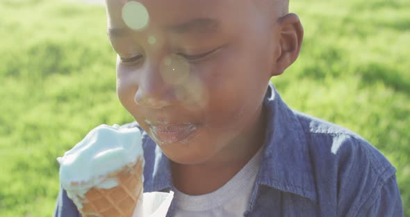 Video of happy african american boy eating ice creams on grass on sunny day