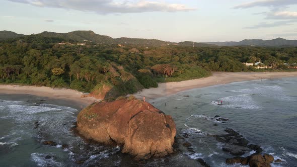 Man standing on the edge of a cliff with his little son. Big rock on a tropical beach with palm tree