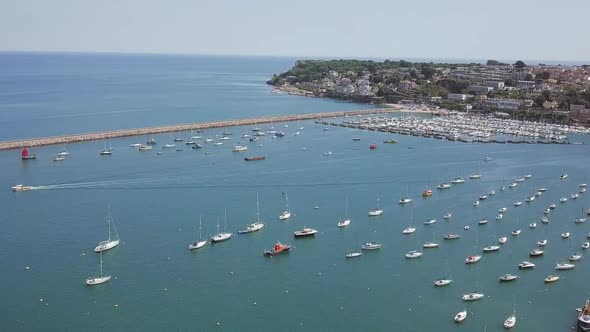 Aerial footage of yachts and sailboats in port of a marina by a seaside community.