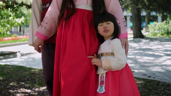 Korean Family in National Costumes in Nature Stands Next to a Cherry Blossoming Tree