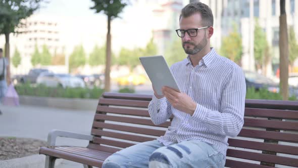 Young Adult Man Using Tablet While Sitting Outdoor on Bench