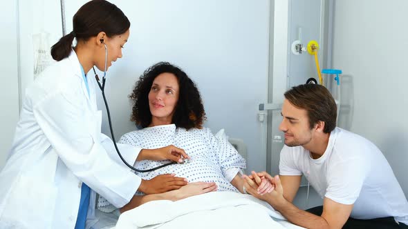 Doctor examining pregnant woman with stethoscope in ward