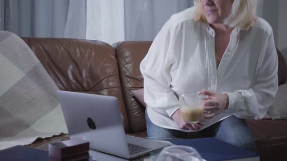 Mature Smiling Caucasian Woman Coming with Cappuccino To Laptop and Looking at Screen