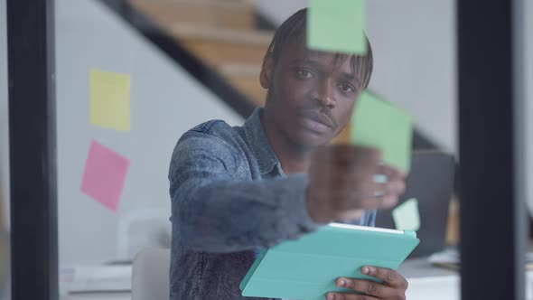 Young Man with Thoughtful Facial Expression Examining Sticky Notes on Glass Door and Online