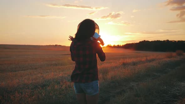 Happy Little Toddler Boy in Hat Having Fun Sitting in Parents Arms in Field in Summer at Sunset