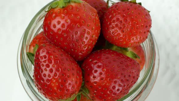 4K glass jar with red ripe strawberries rotating counterclockwise on a white background.