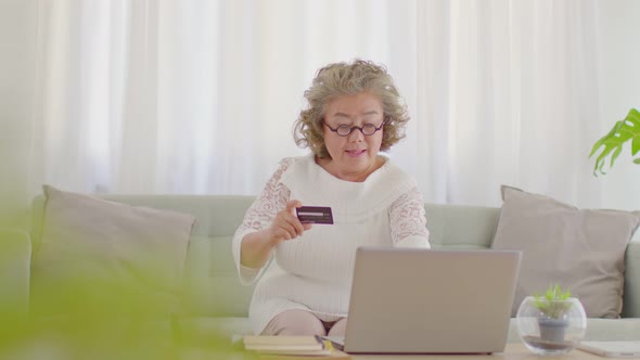 elderly asian woman using computer laptop and credit card to shopping online and payment at home