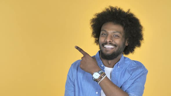 AfroAmerican Man Pointing with Finger on Side Yellow Background