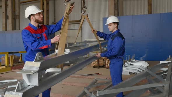 Workers at the Plant Load the Cargo Onto the Hook of the Crane Against the Background of Production